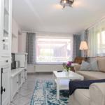 Wohnzimmer mit Sofa, Tisch, Fenstern und Gardinen.