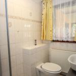 Badezimmer mit Dusche, Toilette und Waschbecken. Fenster mit gelben Vorhängen.