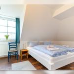 Schlafzimmer mit Doppelbett, Fenster, blauer Stuhl und Holzsideboard.