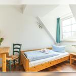 Ein Schlafzimmer mit Holzbett, Tisch, Stuhl und Fenster mit Vorhang.