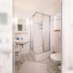 Badezimmer mit Dusche, Waschbecken und Toilette. Fliesenboden und Spiegelschrank.