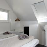 Schlafzimmer mit Dachschrägen, Fenster und Dachfenster. Bett, Kleiderschrank und Heizkörper.