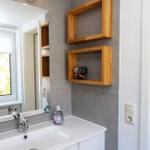 Badezimmer mit Waschbecken, Spiegel und Holzregalen an der Wand.
