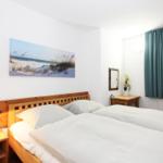 Schlafzimmer mit Doppelbett, Holzbett, Nachttisch und Fenster mit Vorhang.
