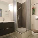 Badezimmer mit Dusche, Waschbecken und Toilette. Wand mit Bild und Blumen.