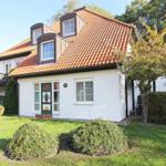 Ein weißes Haus mit rotem Ziegeldach und grüner Haustür im Garten.