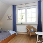 Schlafzimmer mit Dachschräge, Bett, zwei Stühlen und Fenster mit Vorhängen.