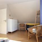Zimmer mit Holzboden, weißen Türen, Wickerstühlen und Kleiderschrank.