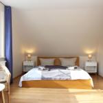 Schlafzimmer mit Doppelbett, zwei Nachttischen und Fenster mit blauen Vorhängen.