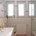 Badezimmer mit Dusche, Waschbecken und drei Fenstern