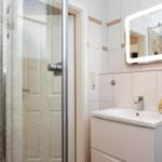 Badezimmer mit Dusche, Waschbecken und beleuchtetem Spiegel