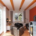 Wohnzimmer mit Holzbalken, roter Wand, Kaminofen und Sitzgelegenheiten.