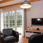 Wohnzimmer mit zwei schwarzen Ledersesseln, TV, Schrank und Fenster zum Garten.