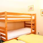 Ein Raum mit einem Holz-Kinderbett und einem Bett mit gelbem Bettzeug.