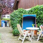 Außenbereich mit Strandkorb, Tisch und Stühlen vor grüner Hecke.