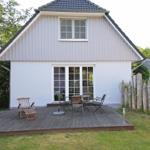 Haus mit Terrasse, Garten und Holzgeländer. Tisch und Stühle auf der Terrasse.