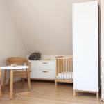 Kinderzimmer mit Babybett, Schrank und Esstisch mit Stühlen.