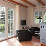 Wohnzimmer mit Sitzgelegenheiten, Fernseher und Kaminofen. Große Fenster mit Blick auf Garten.