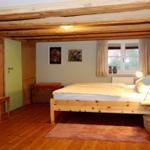 Schlafzimmer mit Holzbalken, Bett, Schreibtisch und Fenster.