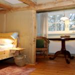Schlafzimmer mit Holzbett, Tisch und Stühlen. Holzdecken und Boden. Fenster mit Vorhängen.