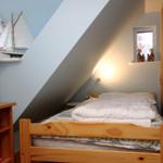 Schlafzimmer mit Holzbett, Nachttisch und Fenster. Wandgestaltung mit Segelschiffmodell.