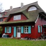 Rotes Haus mit Strohdach, blauen Fensterläden und grünem Garten.
