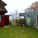Rotes und blaues Gebäude mit grünen Fensterrahmen und roter Tür im Garten.