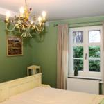 Schlafzimmer mit grüner Wand, Bett, Fenster und Kronleuchter.