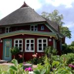 Rotes Haus mit Strohdach und blauer Tür im Garten mit Blumen.