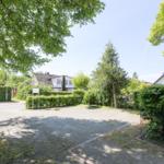 Haus mit gepflegtem Garten und Parkplatz unter Bäumen.