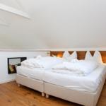 Zimmer mit Doppelbett, Holzboden und Dachschräge. Bücherregale an der Wand.