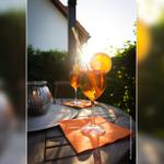 Ein Glas Aperol Spritz auf einer Terrasse mit Sonnenlicht und grüner Umgebung.