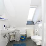 Badezimmer mit Waschbecken, Toilette und Dachfenster. Weiße Fliesen und graue Bodenfliesen.