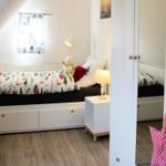 Ein Schlafzimmer mit Dachschrägen, weißem Bett und Nachttisch mit Lampe.