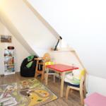 Kinderzimmer mit Spielzeug, Tisch, Stühlen und Teppich unter schrägen Dachschrägen.