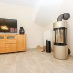 Wohnzimmer mit TV, Holzschrank und Kaminofen an der Wand.