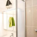 Dusche mit Duschbrause, Spiegelschrank und grünen Handtüchern.