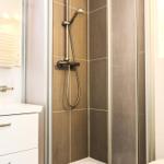 Dusche mit Duschbrause, Waschbecken und Spiegel im Badezimmer.