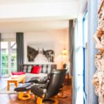 Wohnzimmer mit Sofa, Sessel und Holztisch. Fenster mit Blick auf Garten. Dekorative Baumrinde an Wand.