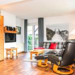 Wohnzimmer mit Sofa, Ledersessel und Holzmöbel. Fenster mit Blick nach draußen.