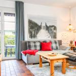 Wohnzimmer mit Sofa, Couchtisch und Sessel. Wandbild zeigt Strandweg. Fenster mit Blick auf Garten.