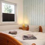 Schlafzimmer mit Holzbett, Fenster und Nachttisch mit Lampe.