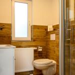 Badezimmer mit Toilette, Dusche und Fenster. Holzwandverkleidung und weißer Waschtisch.