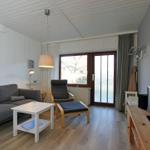 Wohnzimmer mit Sofa, Sessel, Fernseher und Blick auf Wasser.