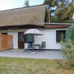 Haus mit strohgedecktem Dach, Terrasse mit Tisch, Stühlen und Sonnenschirm.