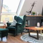 Ein Wohnzimmer mit grünem Sessel, Holztisch und Dachfenster.