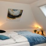 Schlafzimmer mit Dachschräge, Bett, Decke, Nachttische und Fenster.