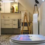 Badezimmer mit Waschbecken, Spiegel und Toilette. Holzregal und Musterboden.
