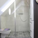 Dusche mit Glaswand, Toilette und schwarz-weißem Bodenfliesenmuster unter Dachschrägen.