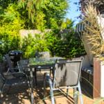 Terrasse mit Tisch, Stühlen, Grill und Strandkorb. Umgeben von grüner Vegetation.